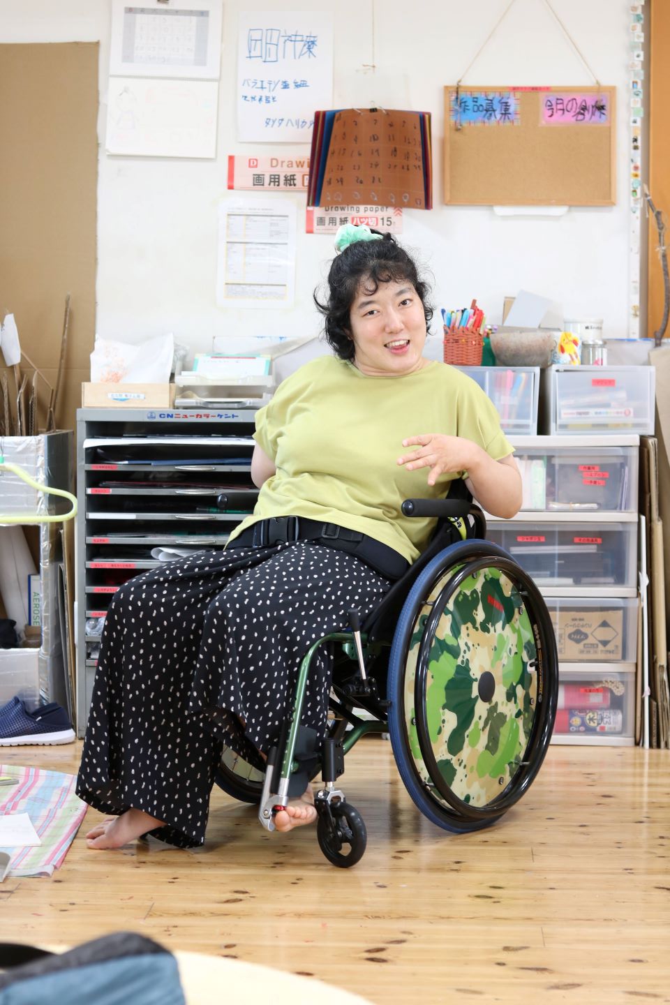 車椅子に乗り、こちらを笑顔で見つめる森さん。背景には使用している制作の道具が見える