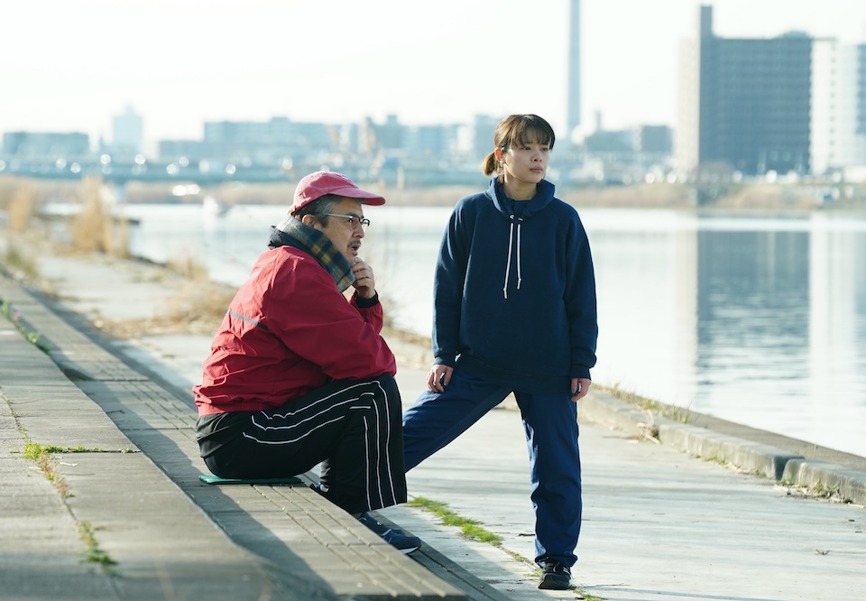 【写真】荒川沿い、昼間。トレーニング服姿のケイコとジムの会長がたたずむ