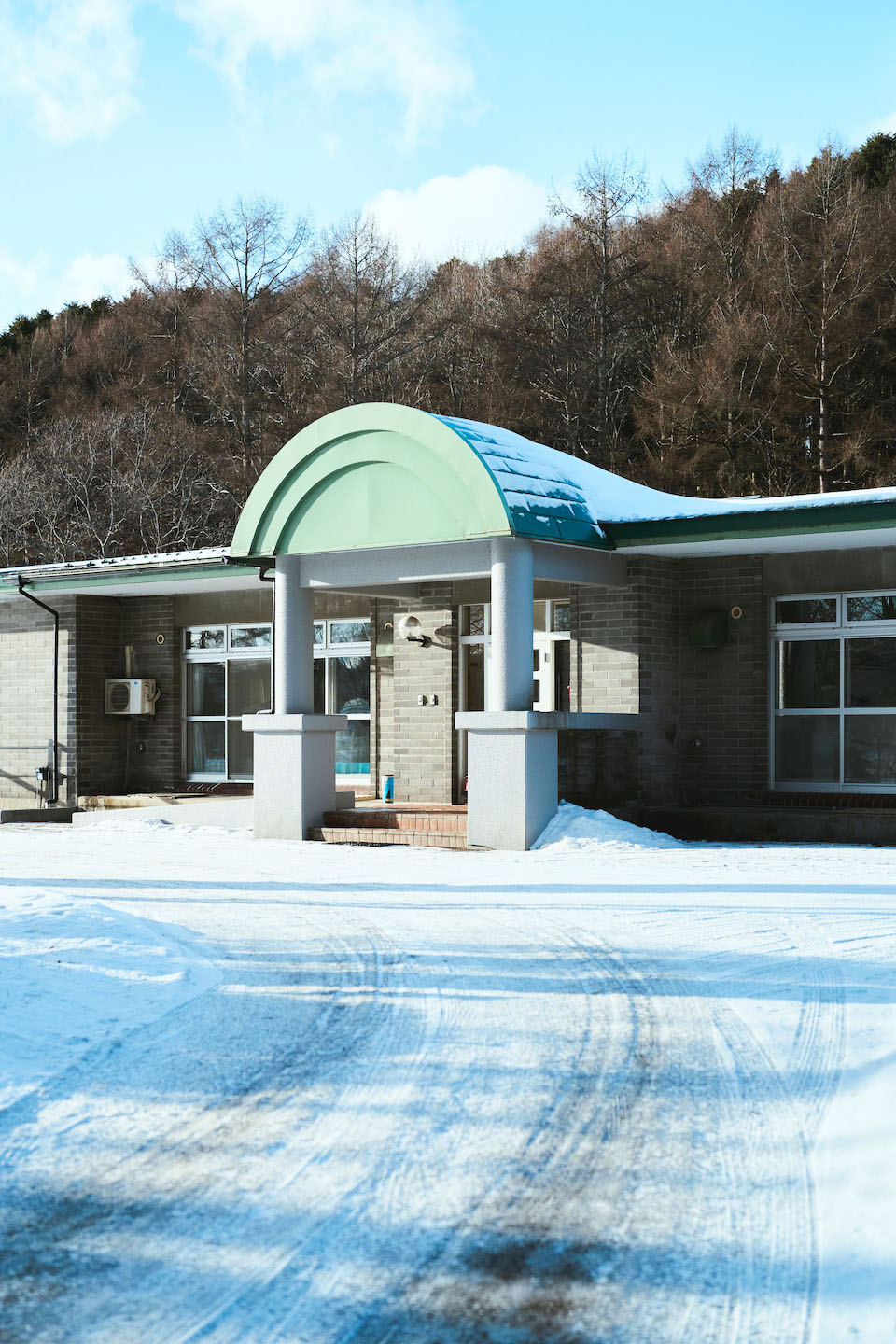 【写真】〈静内桜風園〉の外観。車寄せは雪に覆われ、施設の背景には林がある。